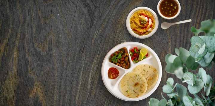White compartment plate with flatbread, curry and salad, alongside bowls of rice and soup on a dark wooden table